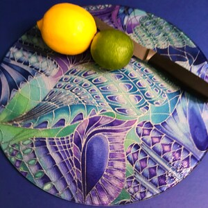 May include: A circular chopping board with an abstract design in blue, purple, and green. A yellow lemon, a green lime, and a knife with a black handle are on the board. The image suggests a kitchen or food preparation setting.