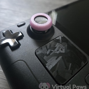 May include: Close-up of a black handheld gaming device with a light purple thumbstick cover. The device has a black cross-shaped directional pad and a patterned square button. The Virtual Paws logo is visible in the bottom right corner.