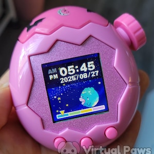 以下が含まれることがあります： 星空のシーンと午前5時45分を表示する画面を備えたピンク色のデジタルペットデバイス。デバイスにはピンク色のボタンとテクスチャ加工された表面があります。