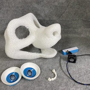 May include: A white 3D-printed animal mask base with a mesh texture, two round eye inserts featuring blue irises, a small white dental piece, a rectangular blue and white block, and a black cooling fan with a connected USB cable and wire.