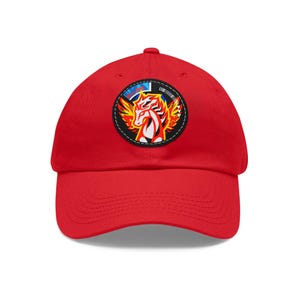May include: A bright red baseball cap featuring a circular patch with a winged horse design in red, orange, and white. The patch is outlined in black with a white stitched border. The cap is made of a soft material.