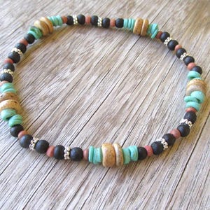 May include: A beaded bracelet featuring black, brown, and turquoise beads. The bracelet is crafted from natural materials and has a simple, elegant design.
