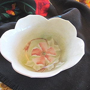 May include: A white porcelain bowl with a floral design. The bowl has a scalloped edge and features a pink flower with green leaves.
