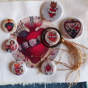 Peut inclure: Ensemble de boutons ronds et un pendentif avec des images de cœurs religieux. Les boutons présentent divers motifs, notamment des cœurs avec des flammes, des couronnes et des éléments floraux. La palette de couleurs comprend le rouge, le blanc et l'or, avec une esthétique vintage.