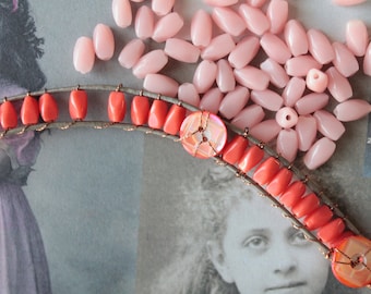 May include: A close-up of a pink and coral beaded necklace with a large, iridescent button. The necklace is made of small, oval-shaped beads and is strung on a wire.