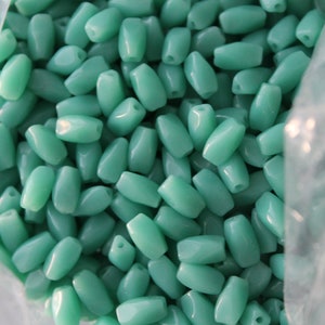 May include: A bag of teal green glass beads. The beads are oval shaped and have a smooth, polished finish.