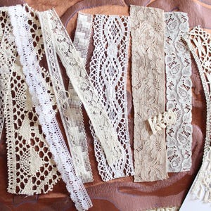 May include: Assortment of white and cream lace trim, featuring various patterns and textures. The lace is arranged on a brown surface.