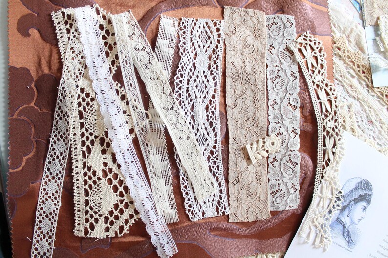 May include: Assortment of white and cream lace trim, featuring various patterns and textures. The lace is arranged on a brown surface.