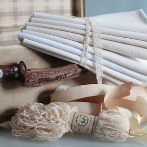 Peut inclure: Une valise vintage remplie de chutes de tissu blanc, de dentelle et de bobines de perles blanches. La valise a une poignée en cuir marron et des fermoirs métalliques.