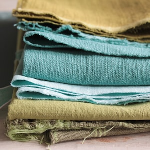 Peut inclure: Un assortiment d'échantillons de tissus dans des tons de vert et de bleu. Le tissu est plié et superposé, révélant différentes textures et motifs.