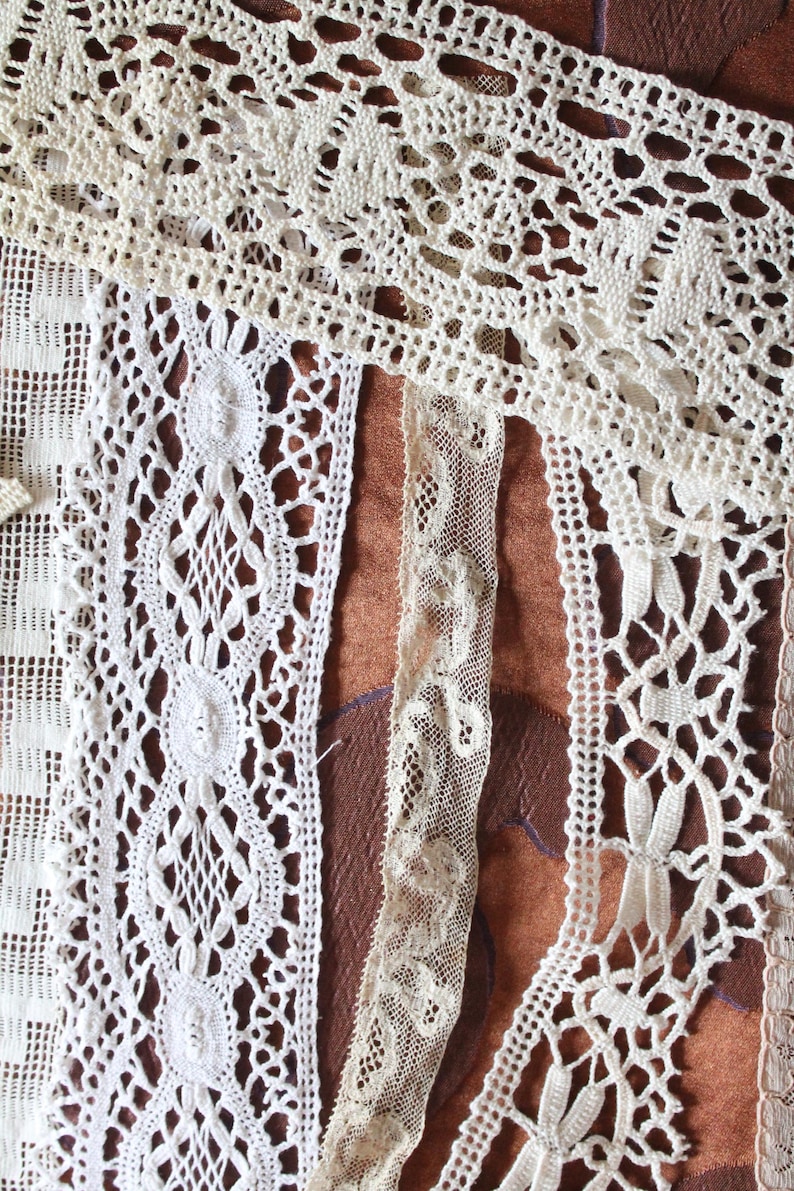 May include: Assortment of white lace trims with different patterns and textures. The lace trims are arranged on a brown surface.