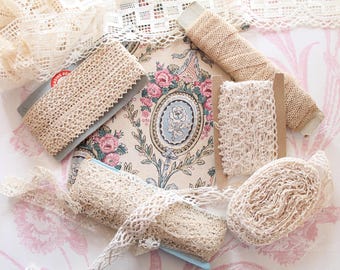 Puede incluir: Una variedad de cintas y adornos de encaje vintage en tonos crema y beige. Algunos están enrollados, otros en carretes o tarjetas, y algunos sueltos. Se aprecia un tejido con estampado floral.
