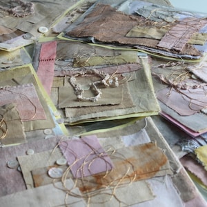 Peut inclure: Un assortiment de pièces d'art en papier faites à la main. Les pièces présentent des textures superposées dans des tons sourds de beige, rose et jaune, avec des accents de fil d'or et de petits boutons blancs. L'esthétique générale est organique et tactile.