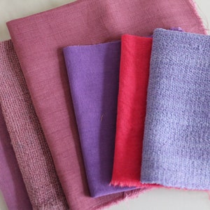 Könnte beinhalten: Eine Sammlung von Stoffmustern in Lila- und Rosatönen. Die Stoffe variieren in der Textur, darunter glatte, gewebte und strukturierte Oberflächen. Die Farbpalette reicht von hellem Lavendel bis zu tiefem Magenta und zeigt eine Vielzahl von Textiloptionen.