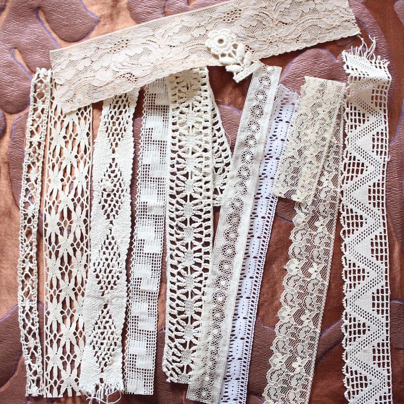 May include: Assortment of white lace trim, featuring various patterns and textures. The lace is arranged in a vertical line on a brown background.