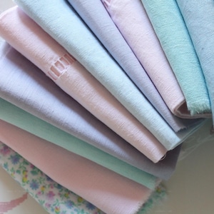 Peut inclure: Une pile de mouchoirs de couleurs pastel, notamment rose clair, lavande, vert menthe et bleu clair. Certains mouchoirs présentent des motifs floraux ou des bords découpés décoratifs. Le tissu semble être du lin ou une matière légère similaire.