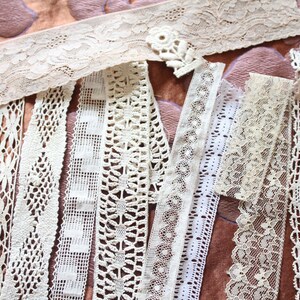 May include: Assortment of white lace trims with various patterns and textures. The trims are arranged in a fan shape on a brown fabric background.