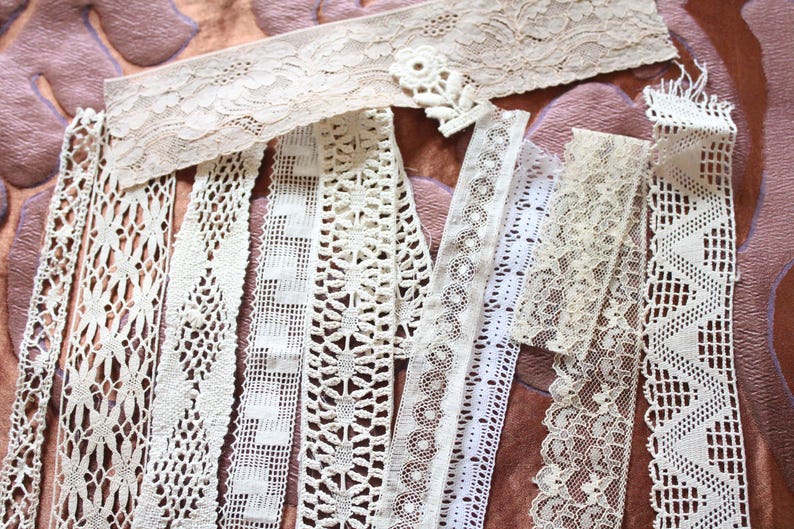 May include: Assortment of white lace trims with various patterns and textures. The trims are arranged in a fan shape on a brown fabric background.