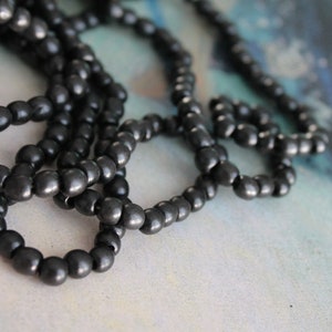 May include: A strand of black beads, possibly made of wood or ceramic, arranged in a loose pile. The beads are round and have a matte finish.