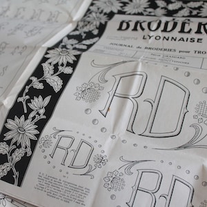 May include: A vintage embroidery pattern sheet with the text "BRODER LYONNAISE" in black. The sheet features floral borders and the letters "RD" in a decorative font, with additional text in French.