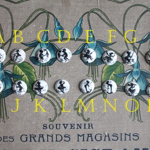 May include: A set of 16 white round buttons featuring black silhouettes of children on bicycles, playing music, and fishing. The buttons are arranged alphabetically from A to P. The buttons are displayed on a beige background with a floral pattern.