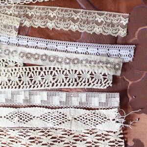 May include: Assortment of white lace trim with various patterns and textures. The lace trim is arranged in rows on a brown fabric background.