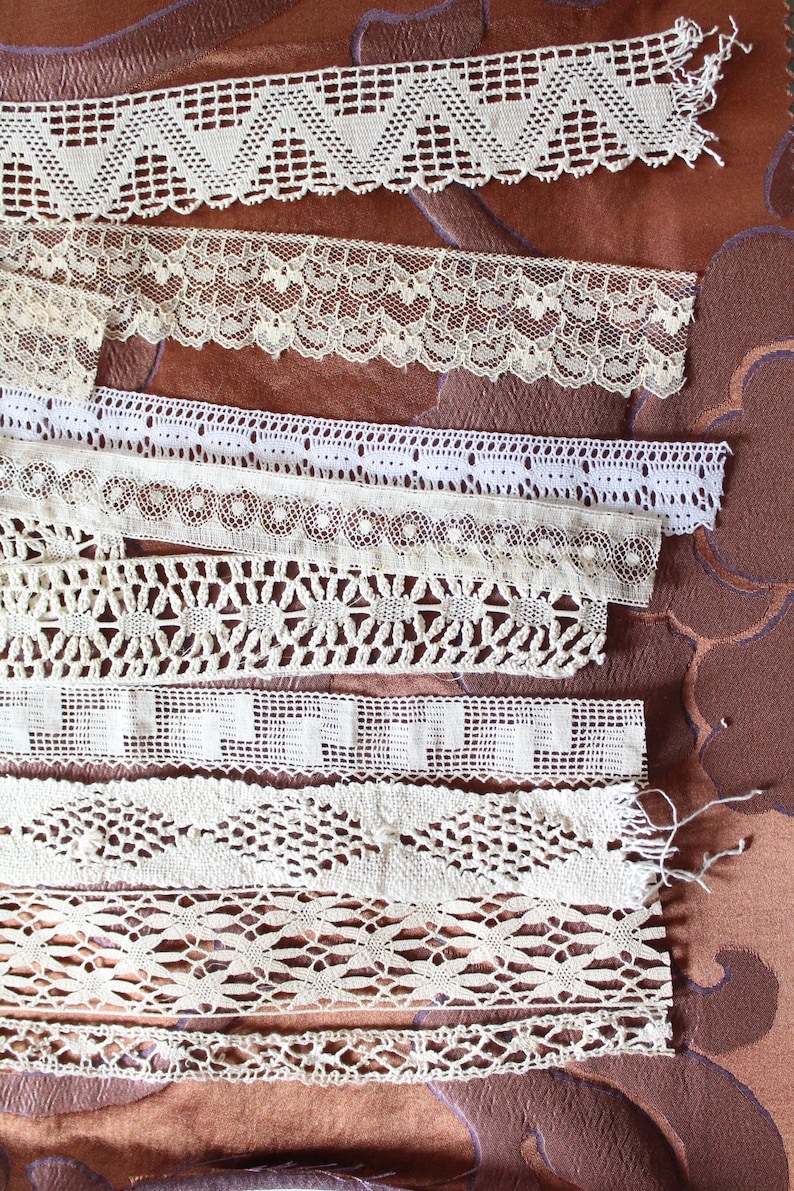 May include: Assortment of white lace trim with various patterns and textures. The lace trim is arranged in rows on a brown fabric background.