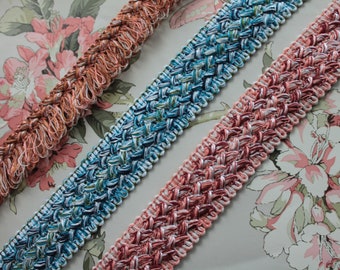 May include: Three different types of trim, one in a peachy pink, one in a blue and green color combination, and one in a brown and white color combination. The trim is woven and has a fringe on one side.
