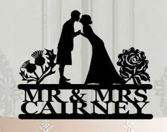 Peut inclure: Topper de gâteau en silhouette noire d'un couple qui s'embrasse avec un chardon et une rose de chaque côté. Le texte "MR & MRS CAIRNEY" est sous le couple.