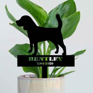 Può includere: Silhouette nera in metallo di un cane con il nome "Bentley" e le date "2001-2020" su una targa nera. La silhouette è posizionata in una pianta in vaso.