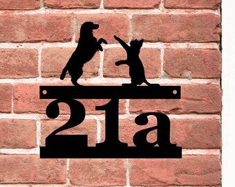 May include: Black metal house number sign with the number 21a. The sign features a silhouette of a dog and cat playing on top of the number.