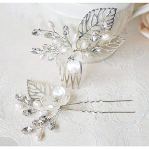 May include: Two elegant bridal hair accessories. One is a comb with a floral and leaf design, adorned with pearls and crystals. The other is a hairpin with a similar floral arrangement, perfect for weddings or special occasions.