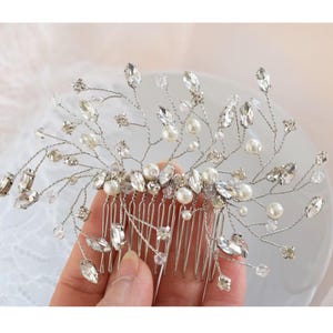 May include: A silver-toned hair comb with a delicate design. It features clear crystals, faux pearls, and wire branches. The comb is designed for formal occasions, such as weddings or proms.