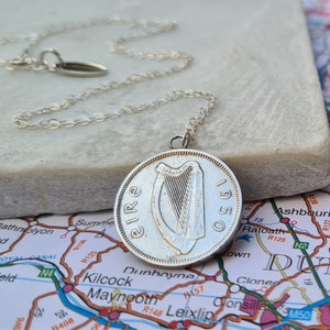 May include: A silver chain necklace with a silver Irish coin pendant featuring a harp and the text "Eire 1950".
