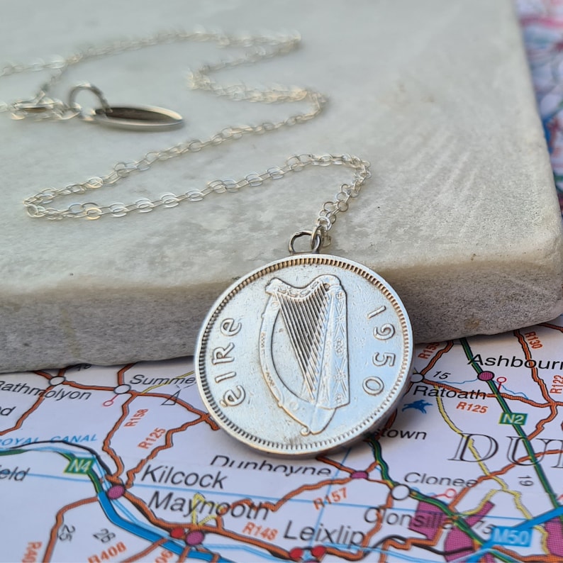 May include: A silver chain necklace with a silver Irish coin pendant featuring a harp and the text "Eire 1950".