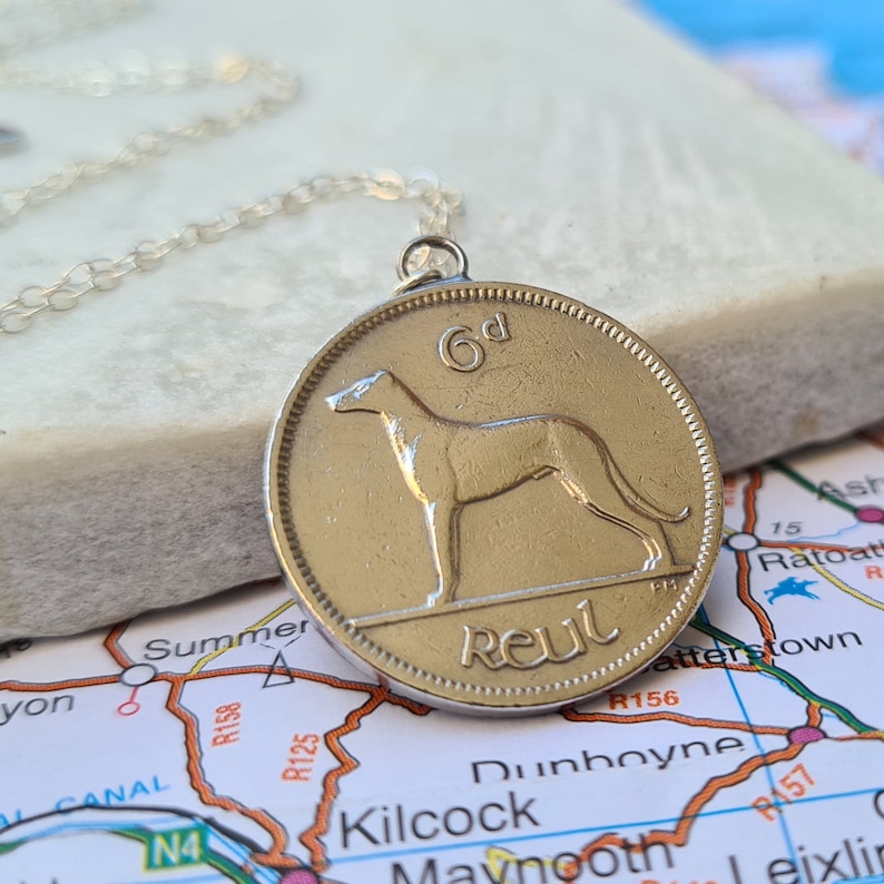 May include: A silver chain necklace with a gold-colored Irish 6d coin pendant featuring a greyhound dog and the word "Reul".