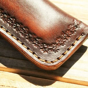 May include: Close-up of a brown leather sheath with a decorative stitch pattern around the edge.