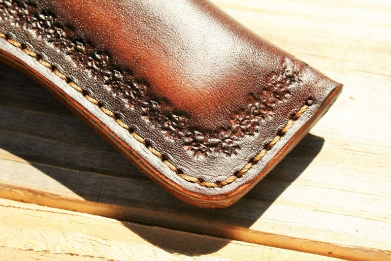May include: Close-up of a brown leather sheath with a decorative stitch pattern around the edge.