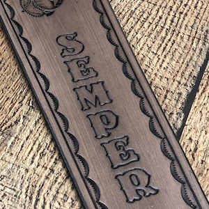 May include: A brown leather guitar strap with a black outline of the Marine Corps emblem and the word "SEMPER FI" in a decorative font.
