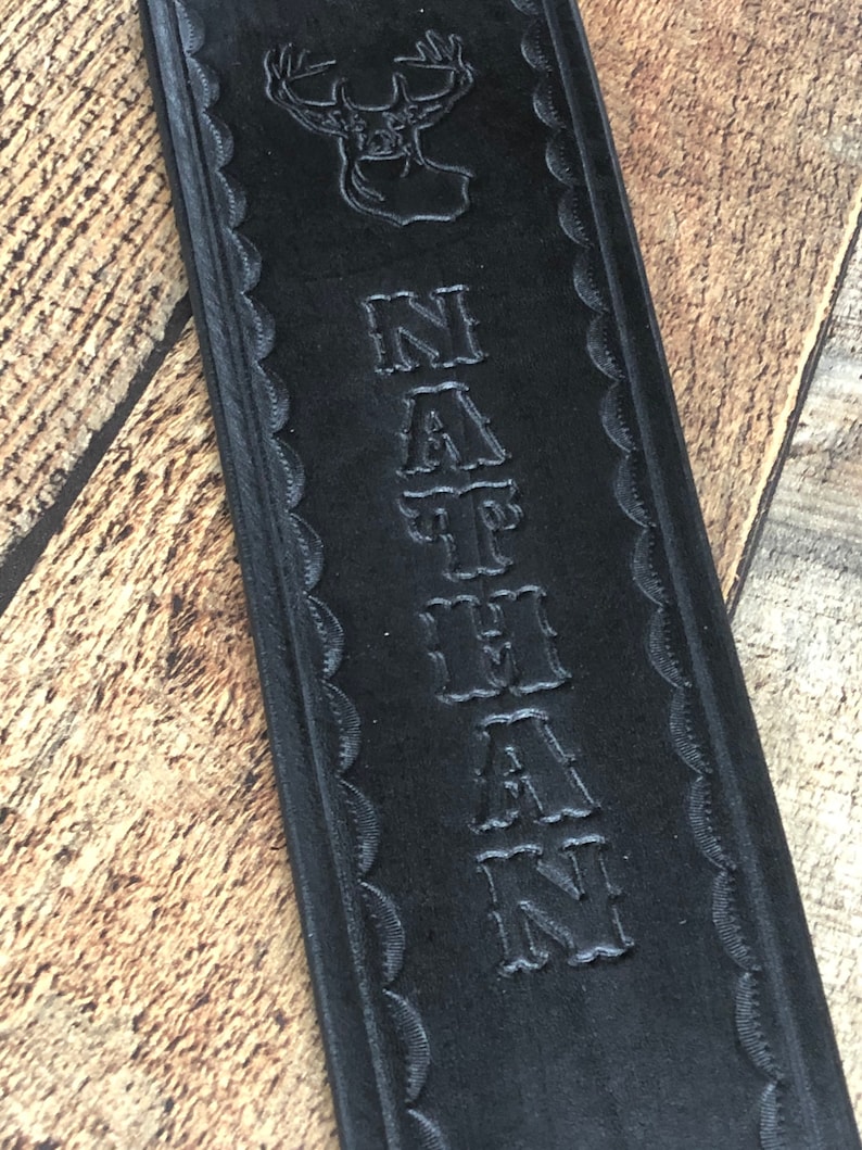 May include: Black leather strap with a deer head design and the name "NATHAN" embossed in a decorative font.