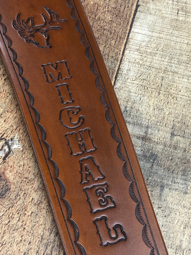May include: Brown leather strap with a decorative border and the name "MICHAEL" embossed in a vintage font. A deer head is also embossed at the top of the strap.