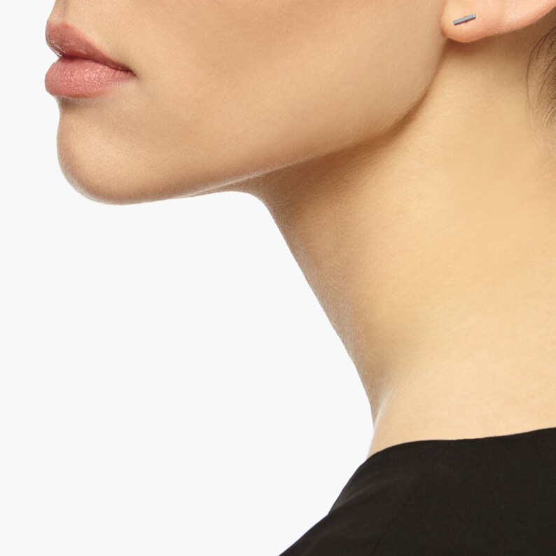 May include: A close-up of a person's face and neck, showing a small, thin, silver bar earring in their right ear.