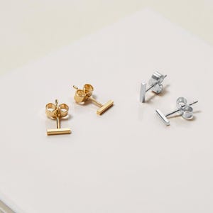 May include: Two pairs of minimalist bar stud earrings. One pair is gold and the other is silver.