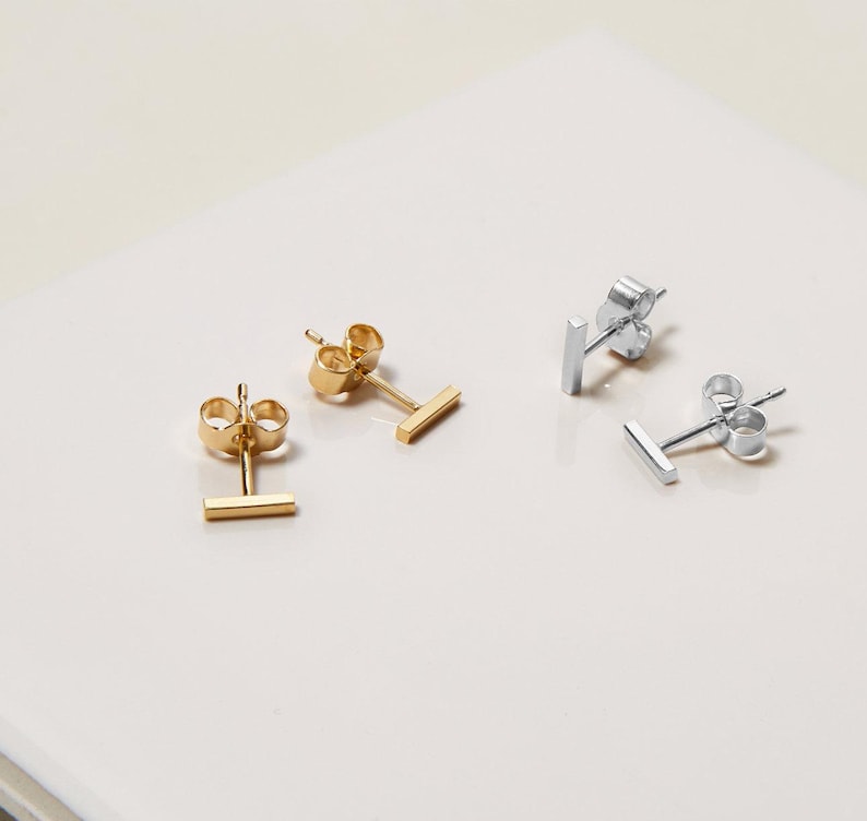 May include: Two pairs of minimalist bar stud earrings. One pair is gold and the other is silver.