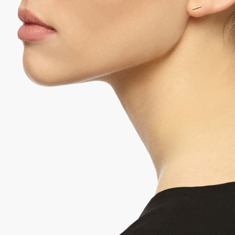 May include: A close-up of a person's ear with a small gold bar earring.