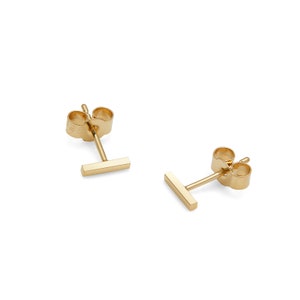 May include: A pair of gold bar stud earrings. The earrings are simple and minimalist, with a small, rectangular bar that hangs from a post.