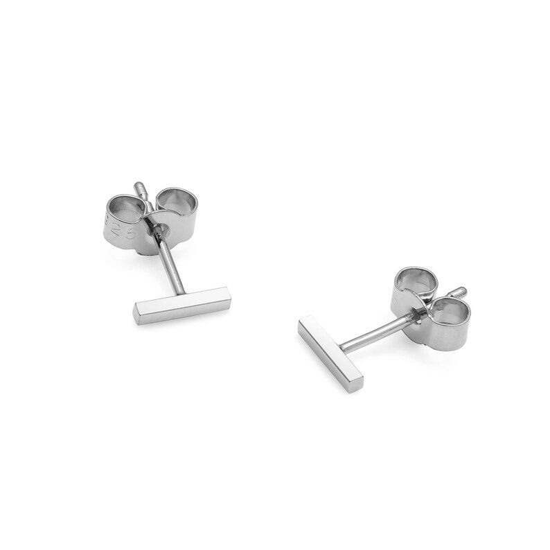 May include: A pair of silver bar stud earrings. The earrings are simple and minimalist, with a small, rectangular bar.