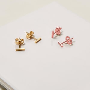 May include: Two pairs of minimalist bar earrings. One pair is gold and the other is rose gold.