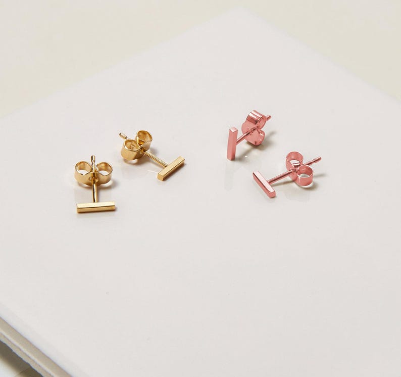 May include: Two pairs of minimalist bar earrings. One pair is gold and the other is rose gold.