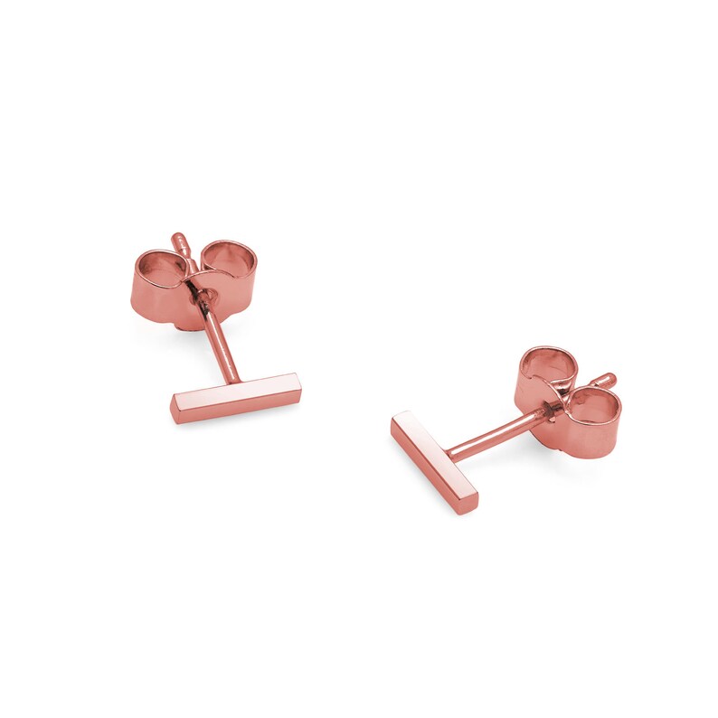 May include: A pair of rose gold stud earrings with a small, horizontal bar design.
